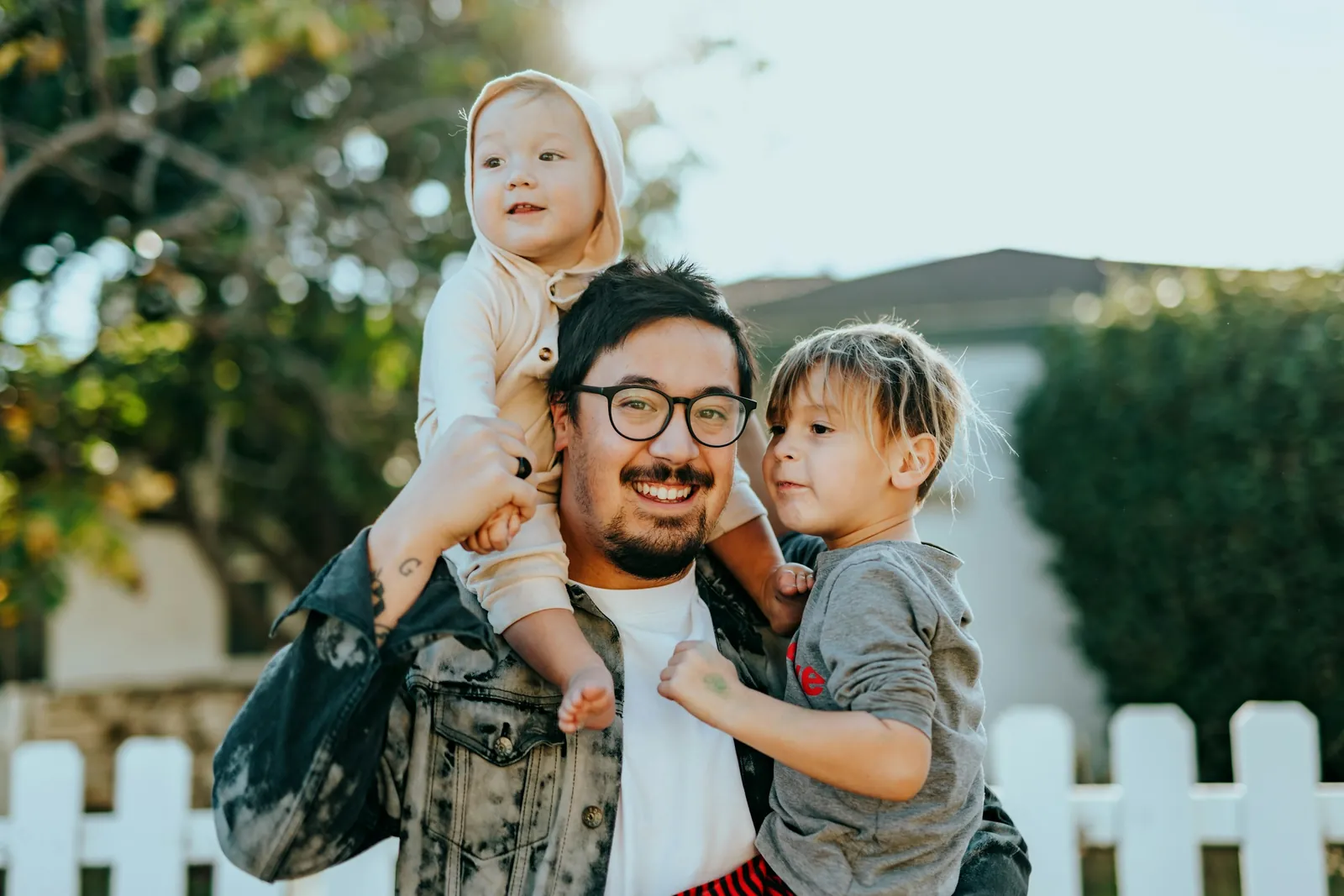 Exemple de photo de naissance : un papa porte son bébé sur les épaules, le grand frère à côté